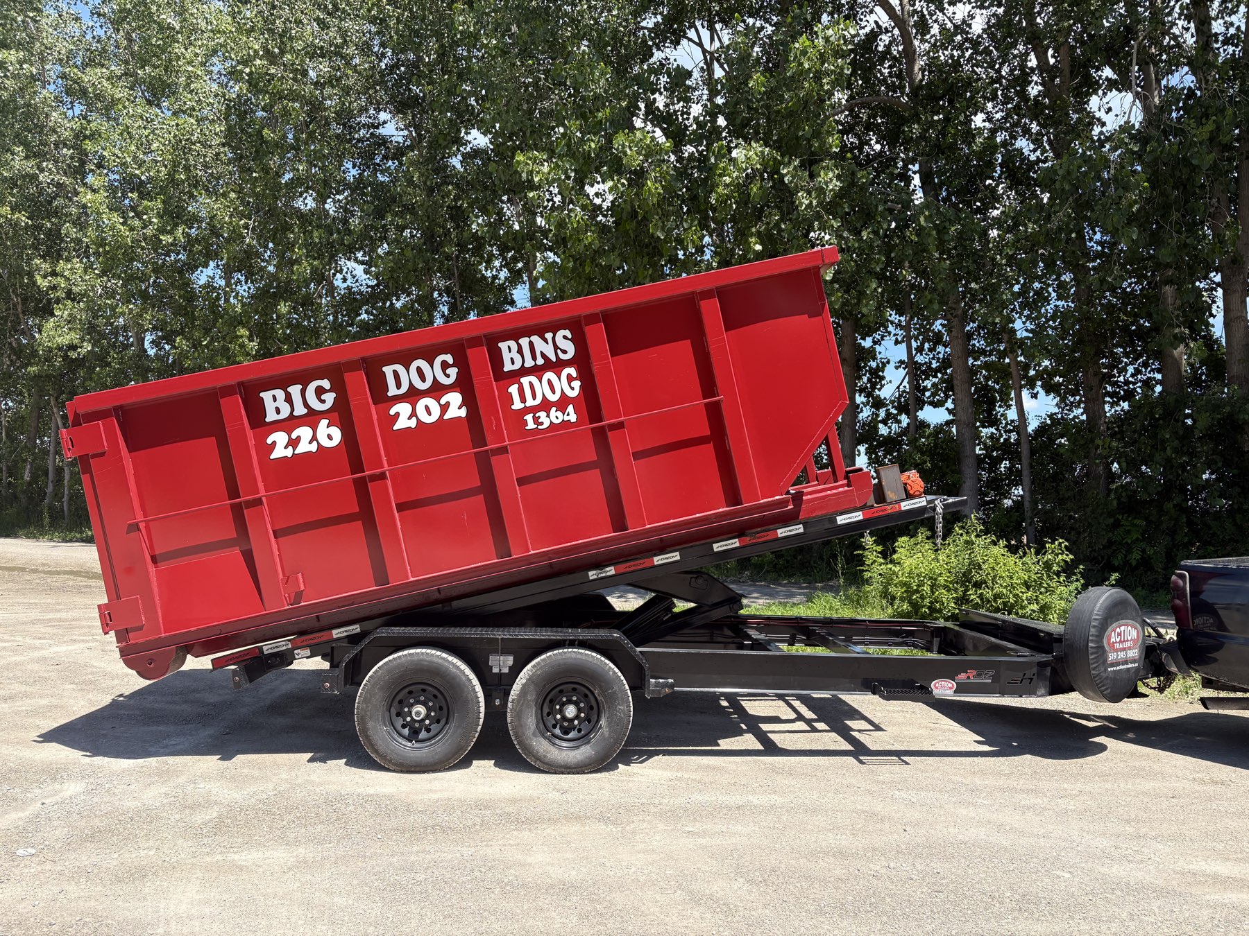 A bright red Big Dog Bins dump bin tilted on a trailer, ready to drop.